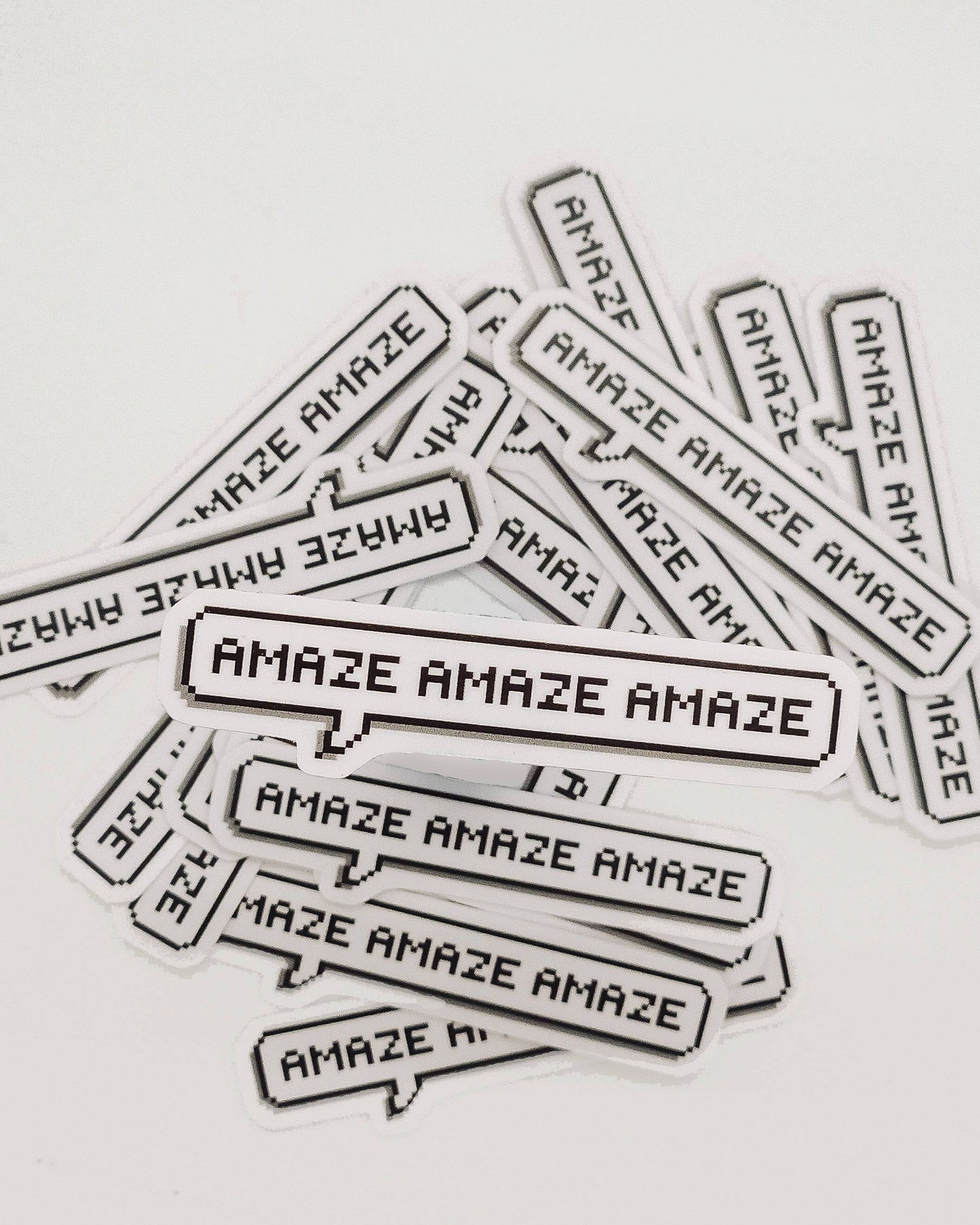 Multiple 'AMAZE' stickers scattered on a light gray background