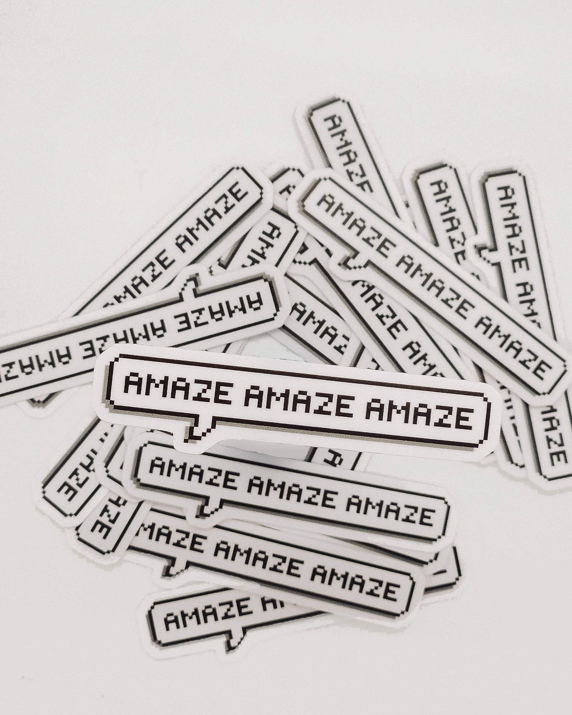 Multiple 'AMAZE' stickers scattered on a light gray background